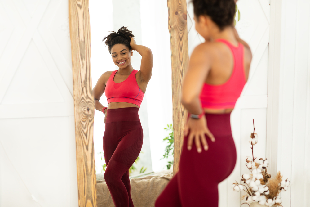 Woman looking happily in the mirror after losing weight with semaglutide or tirzepatide.